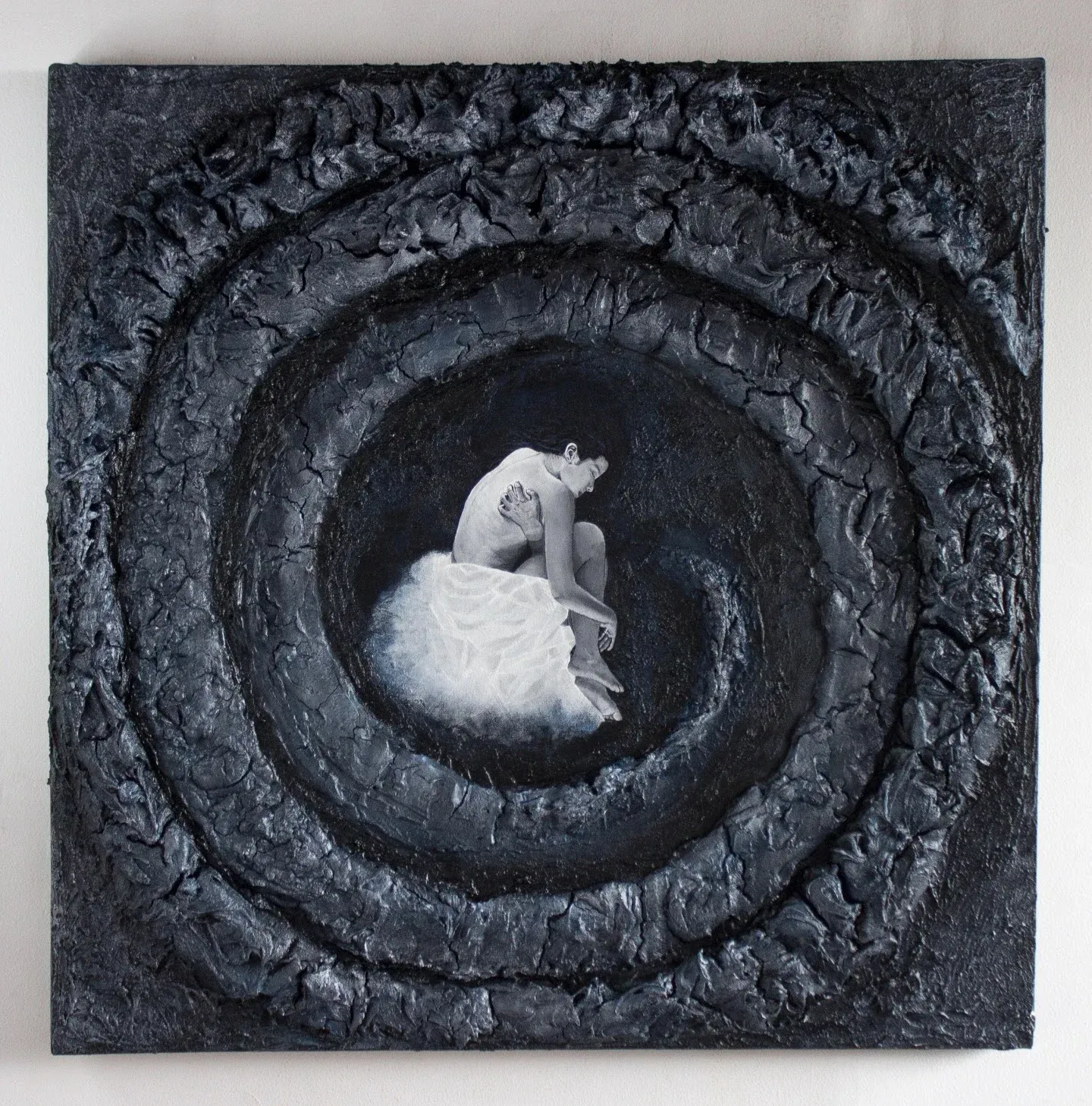 Figura humana encogida en blanco y negro en el centro de una espiral oscura en relieve