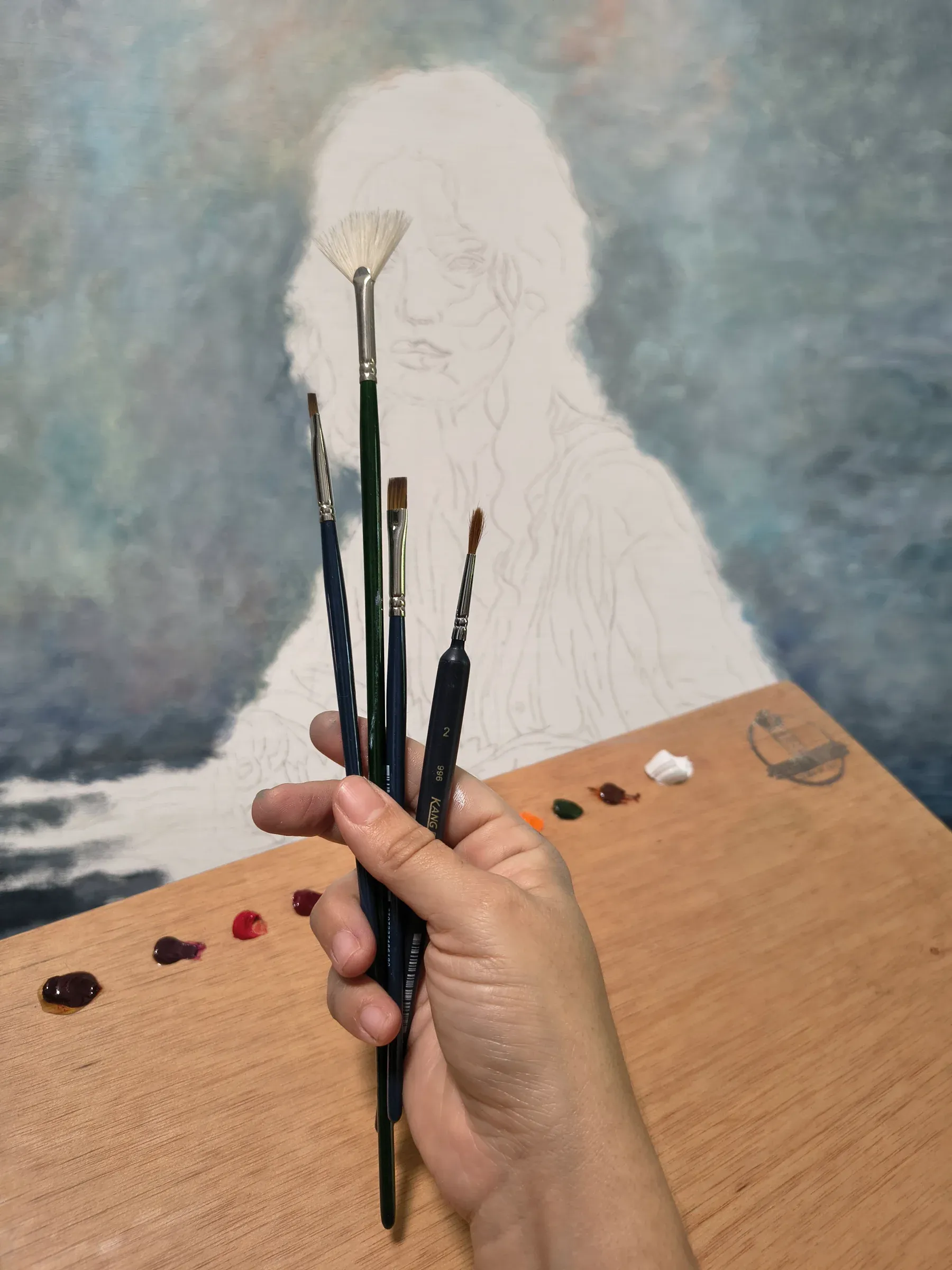 Mano sosteniendo pinceles frente al boceto del retrato